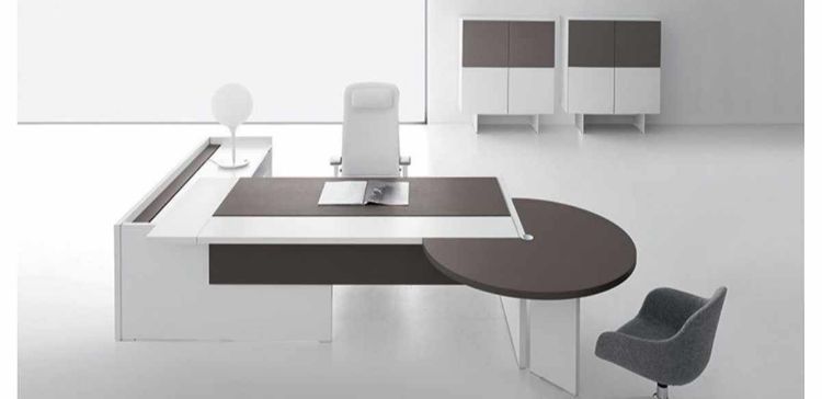 Composizione direzionale con scrivania dotata di piano scorrevole lato operatore, modesty panel in melaminico cappuccino o nocciola, piano fisso con spazzolina nera per gestione cavi, mobile di servizio portante con anta scorrevole soft-closing e serratura, e penisola con gamba per riunioni brevi o attività collaborative.
