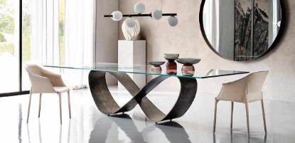 Tavolo sagomato con piano in appoggio in cristallo spessore 15 mm, disponibile in versione trasparente, extrachiaro o extrachiaro con bordi bisellati inversi, base in acciaio titanio, bronzo o finiture Brushed Bronze e Brushed Grey per sale riunioni e ambienti direzionali.